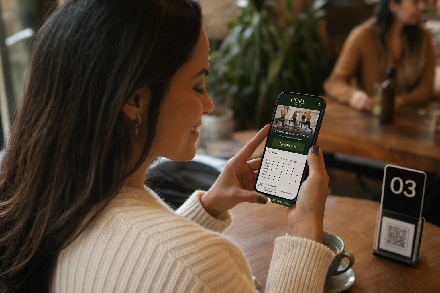Aluna olhando a Página do Estabelecimento de uma academia no celular em uma cafeteria